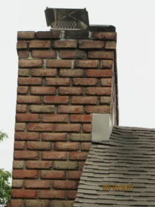Old brick chimney with signs of disrepair and a metallic cap