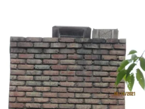 An old brick chimney with visible disrepair and metal flue caps on top.