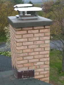 A freshly repaired brick chimney with a metal cap on a shingled roof.