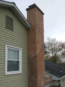 A newly repaired brick chimney on the side of a house with light green siding.