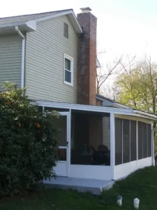 Old, weathered brick chimney on the side of a house with a screened porch.