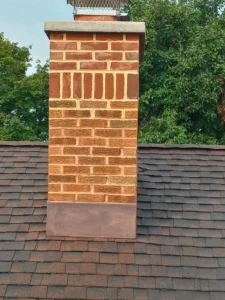 Brick chimney with metal chimney cap on a shingled roof.