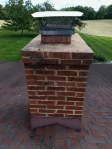 An aging brick chimney in Grantville showing significant weathering and obsolete brick patterns, with multiple metal mesh caps and visible mortar erosion near the roofline.