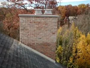 Repaired chimney with metal caps against a backdrop of fall trees.