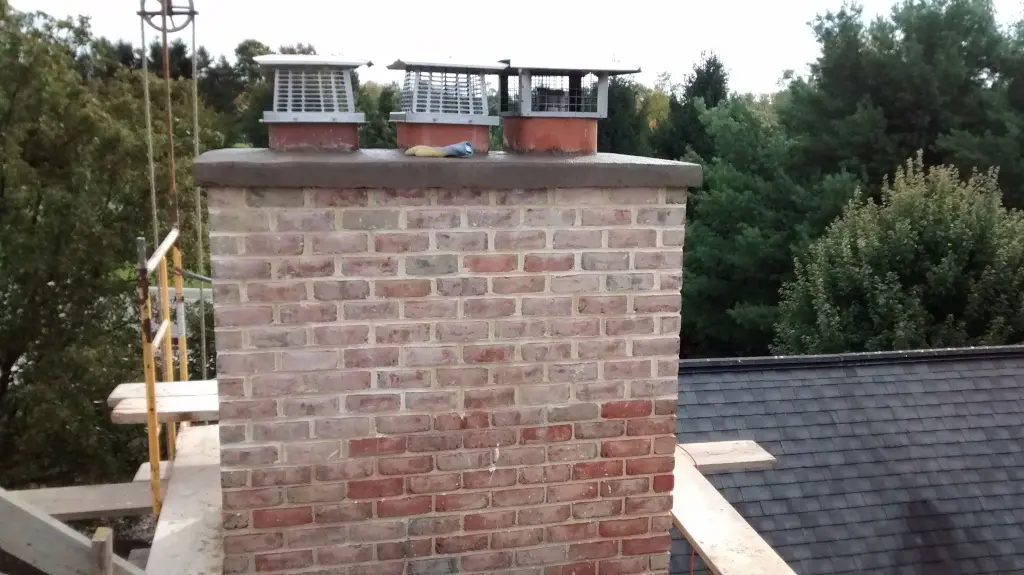 An old brick chimney with disrepair, featuring metal flue caps and signs of erosion.