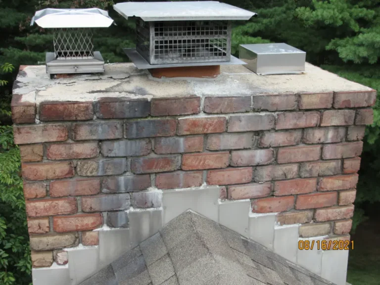 A wide shot of a weathered red-brick chimney showing cracked mortar joints and aging bricks, topped with two metal rain caps